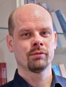 Porträt von Jeroen van den Brink mit ernstem Blick und Hintergrundregal.